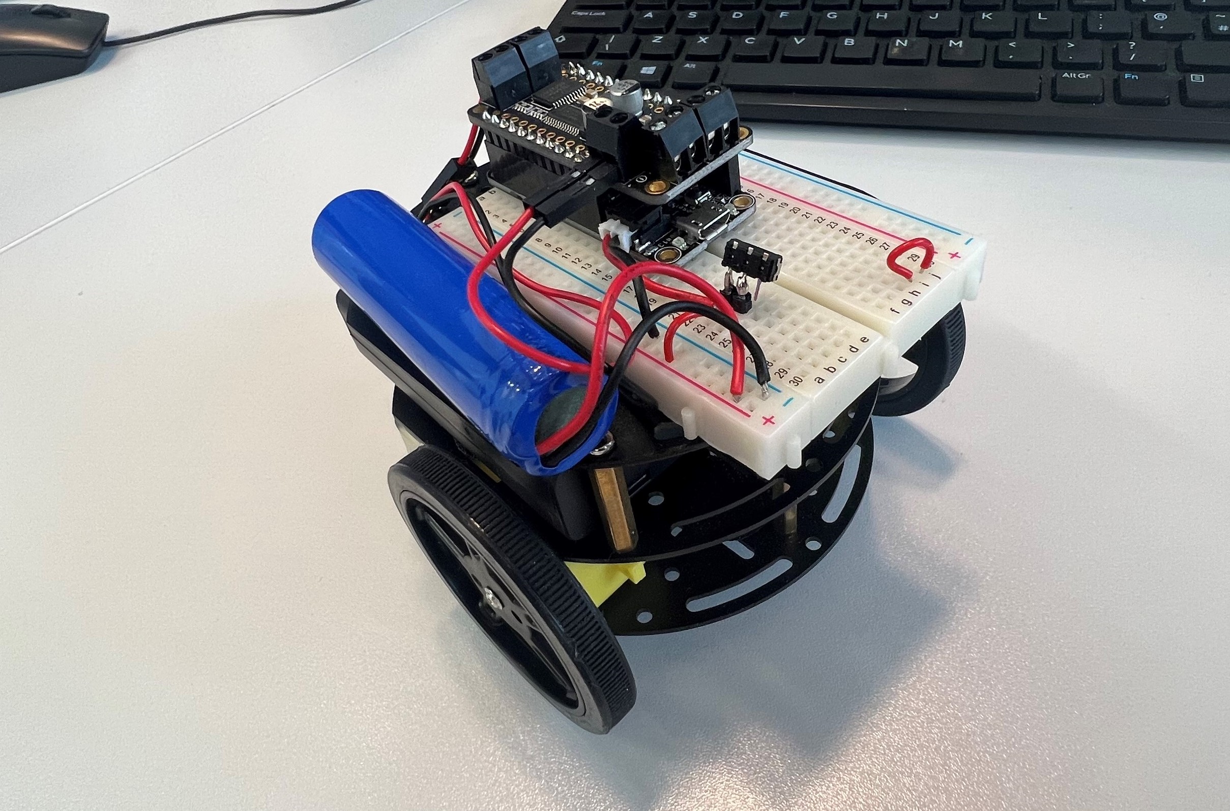 Small Arduino car with a circuit board and battery on top.